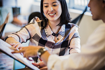 Two coworkers talking and smiling while using a laptop at an office.