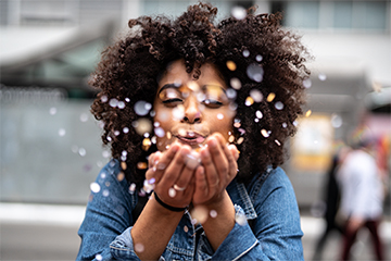 Happy person blowing confetti in an outdoor setting.