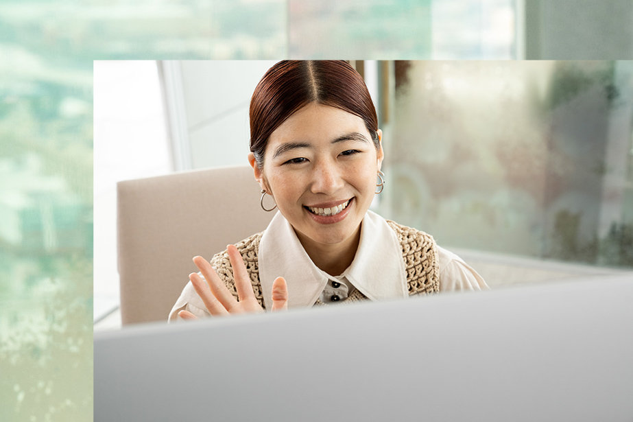 A person smile and waves at the screen of Surface Studio 2+.