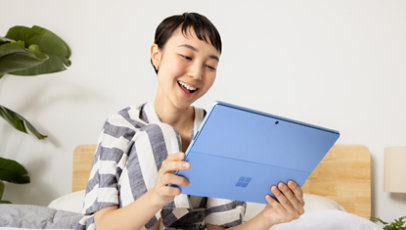 A person smiling while holding a sapphire Surface Pro 9 tablet