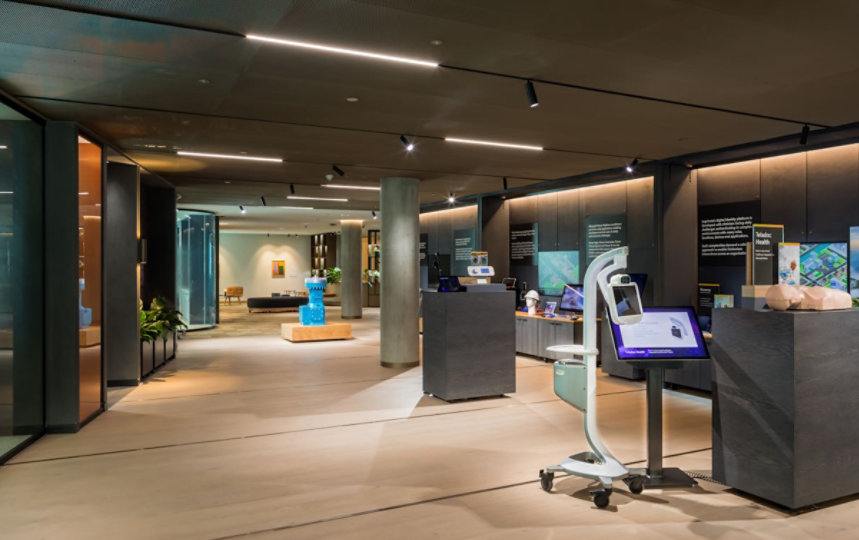 London experience zone - wide shot of an area with dark wood walls, light wood floor, containing demonstration props such as a bright blue industrial pump and a telemedicine machine on casters.