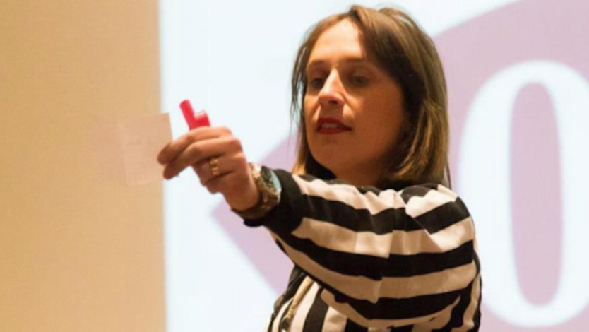 Severine Guilliet in a black and white striped with an outstretched arm holding a small piece of paper