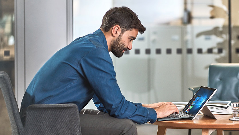 A man in business attire uses a Surface device at a table.