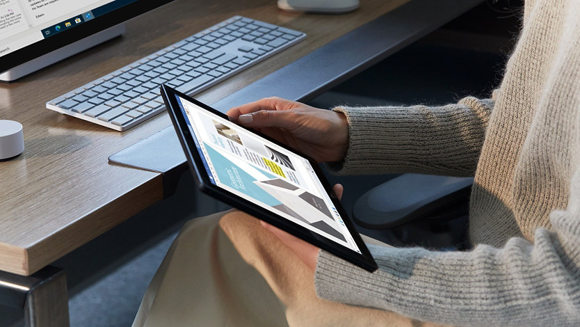 A person sits at a desk with a tablet in hand.